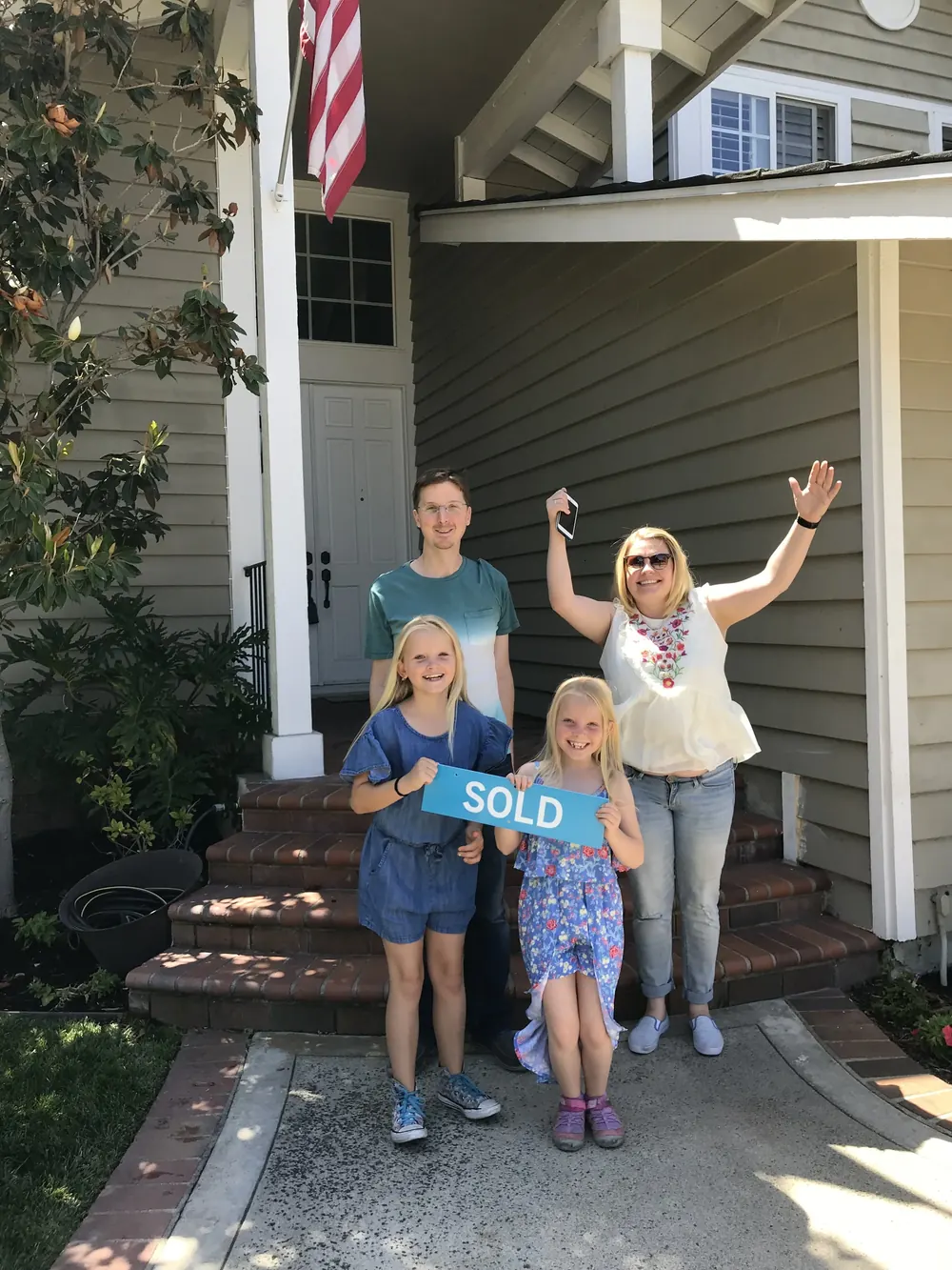 Family celebrating in front of their new home with a SOLD sign