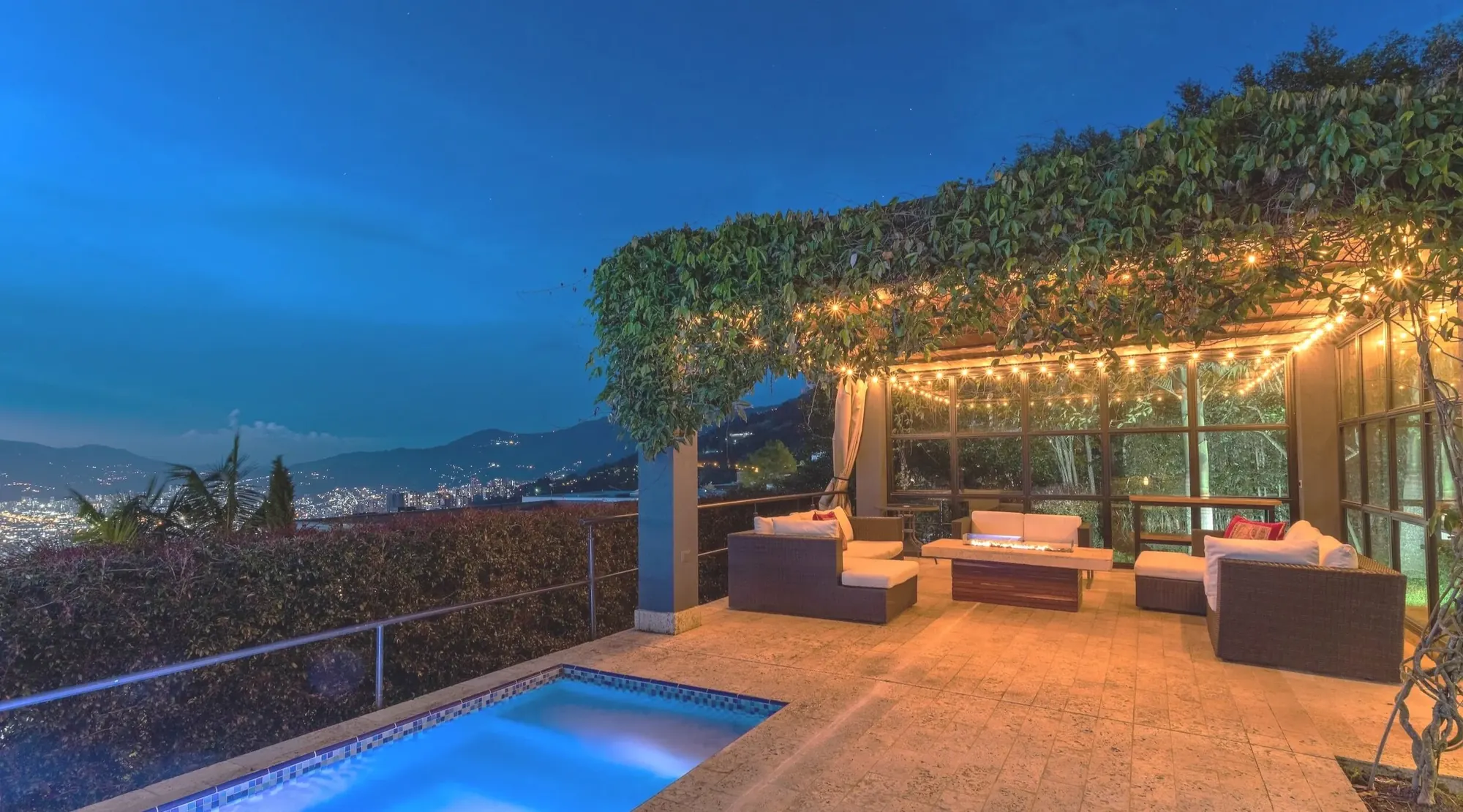 Covered patio with string lights and a plunge pool overlooking the city at dusk